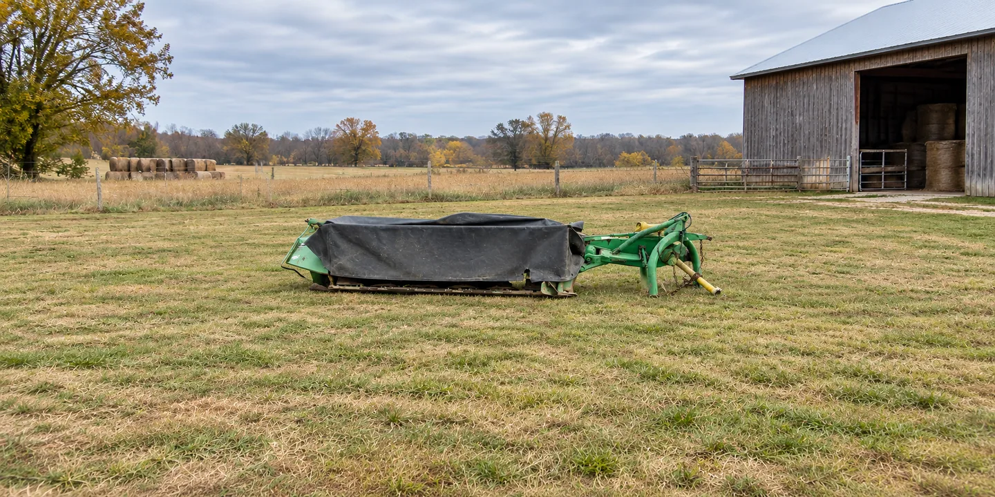 John Deere 260 disc mower — parked on grass beside a hay barn with the protective curtain lowered.